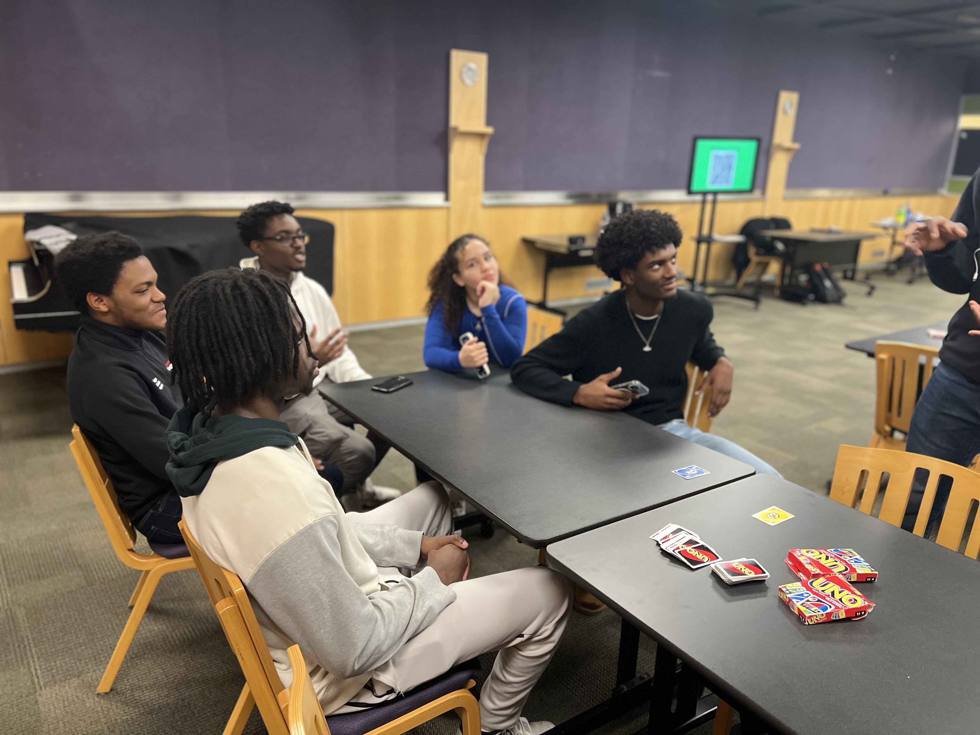 This image slider contains images of NSBE-CU's First-Year Game Night event. The first image of this slider depicts several NSBE members sitting at a small table and talking amongst each other.