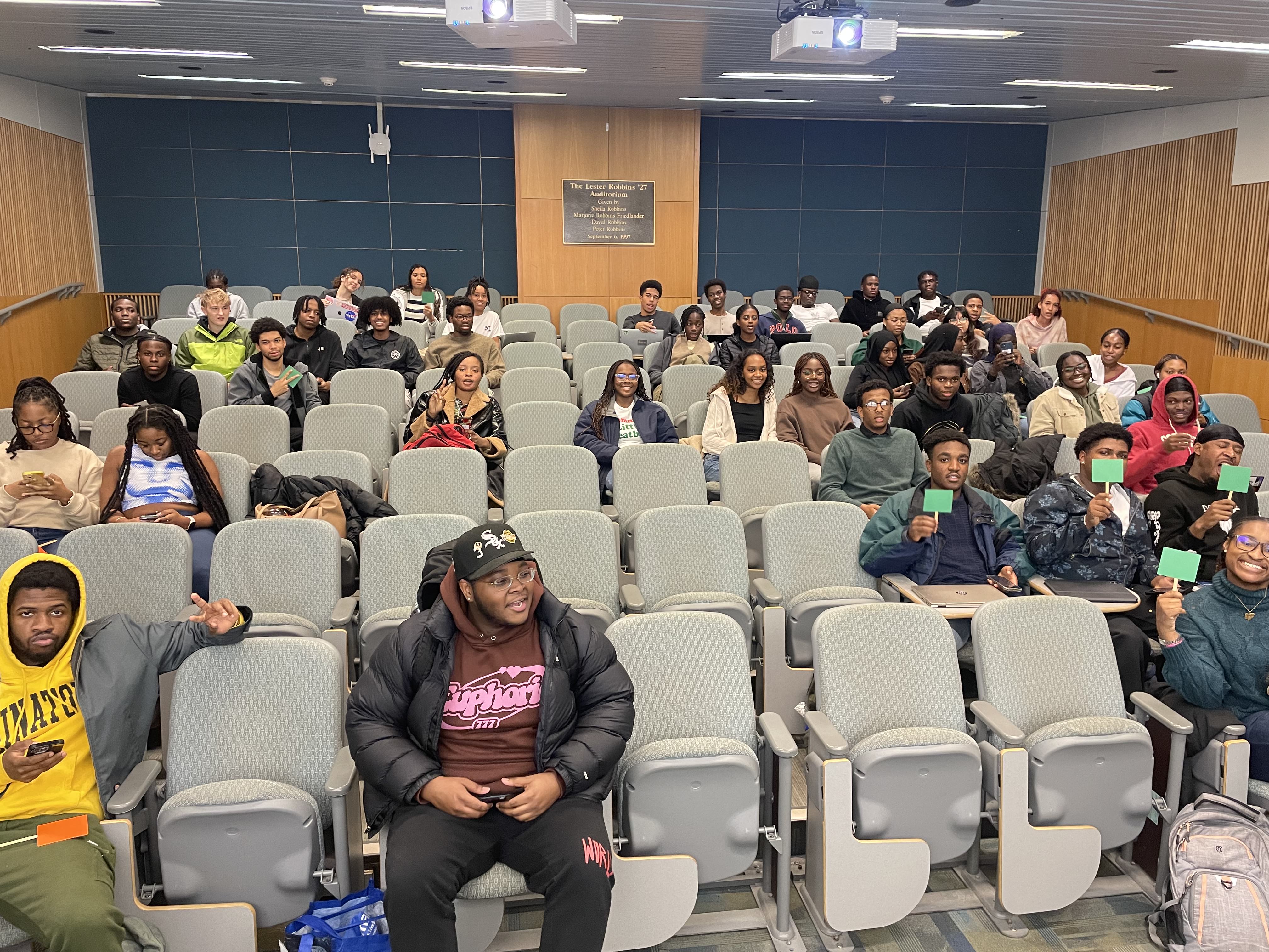 This image slider contains images of NSBE-CU's Hot Takes Social event. The first image of this slider depicts several NSBE members sitting together in a small lecture hall, posing for a picture.