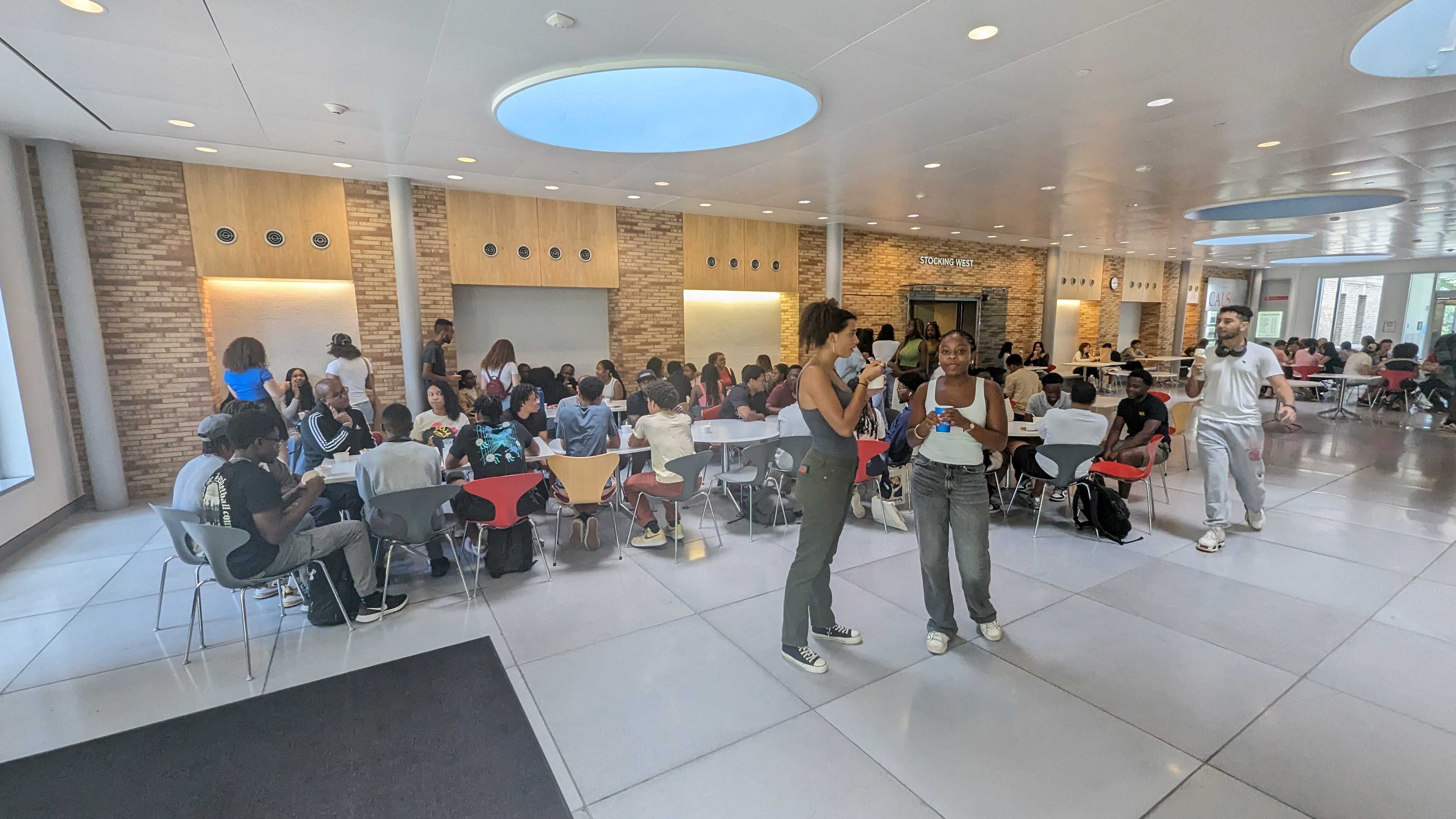 This image slider contains images of NSBE-CU's Ice Cream Social event. The first image of this slider displays a group of students sitting at the Cornell Dairy Bar, sitting at several tables and conversing amongst each other.