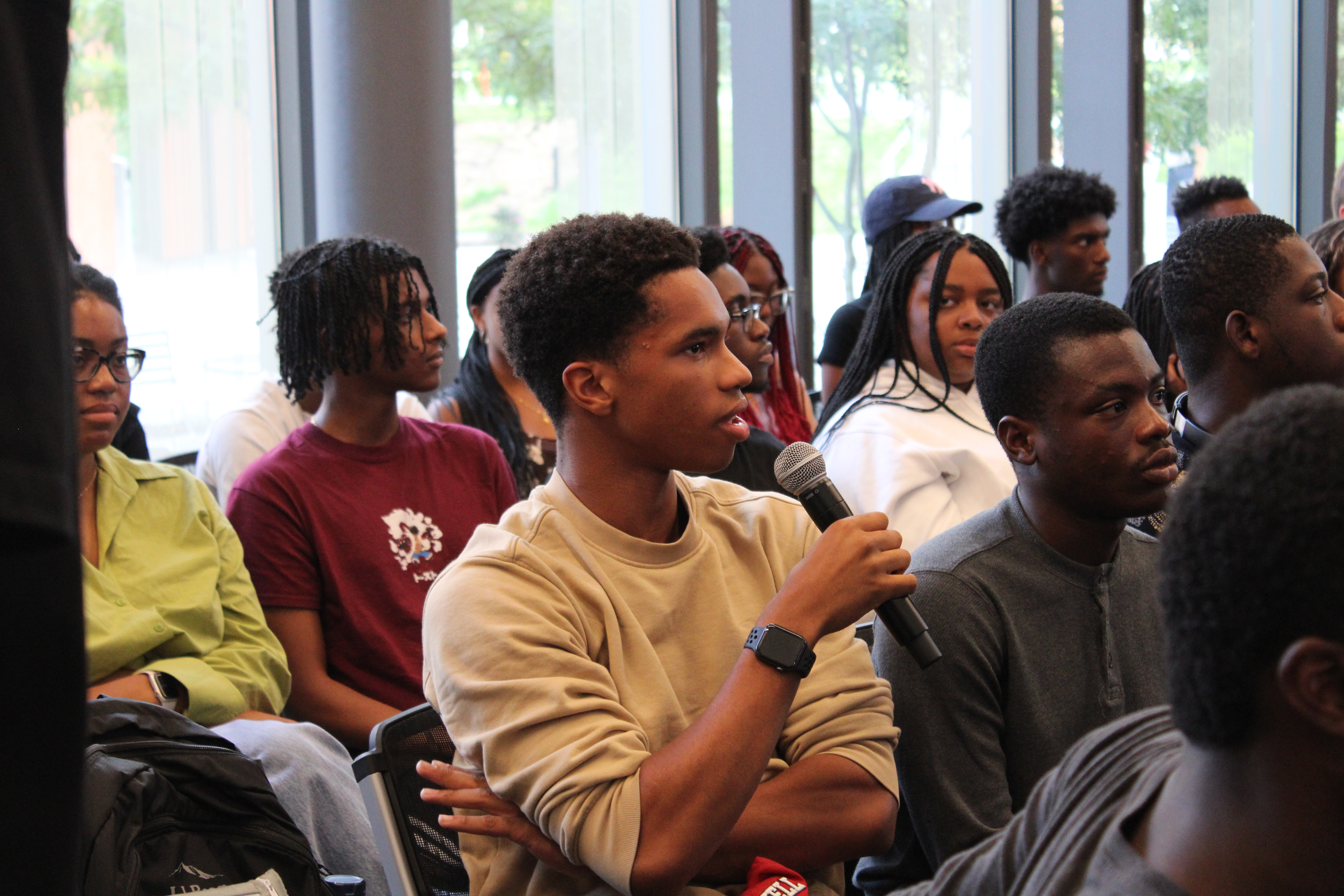 This image slider contains images of NSBE-CU's NSBE101 Information session. The first image of this slider depicts a NSBE-CU general body member, sitting amongst other students, who is speaking aloud using a microphone.