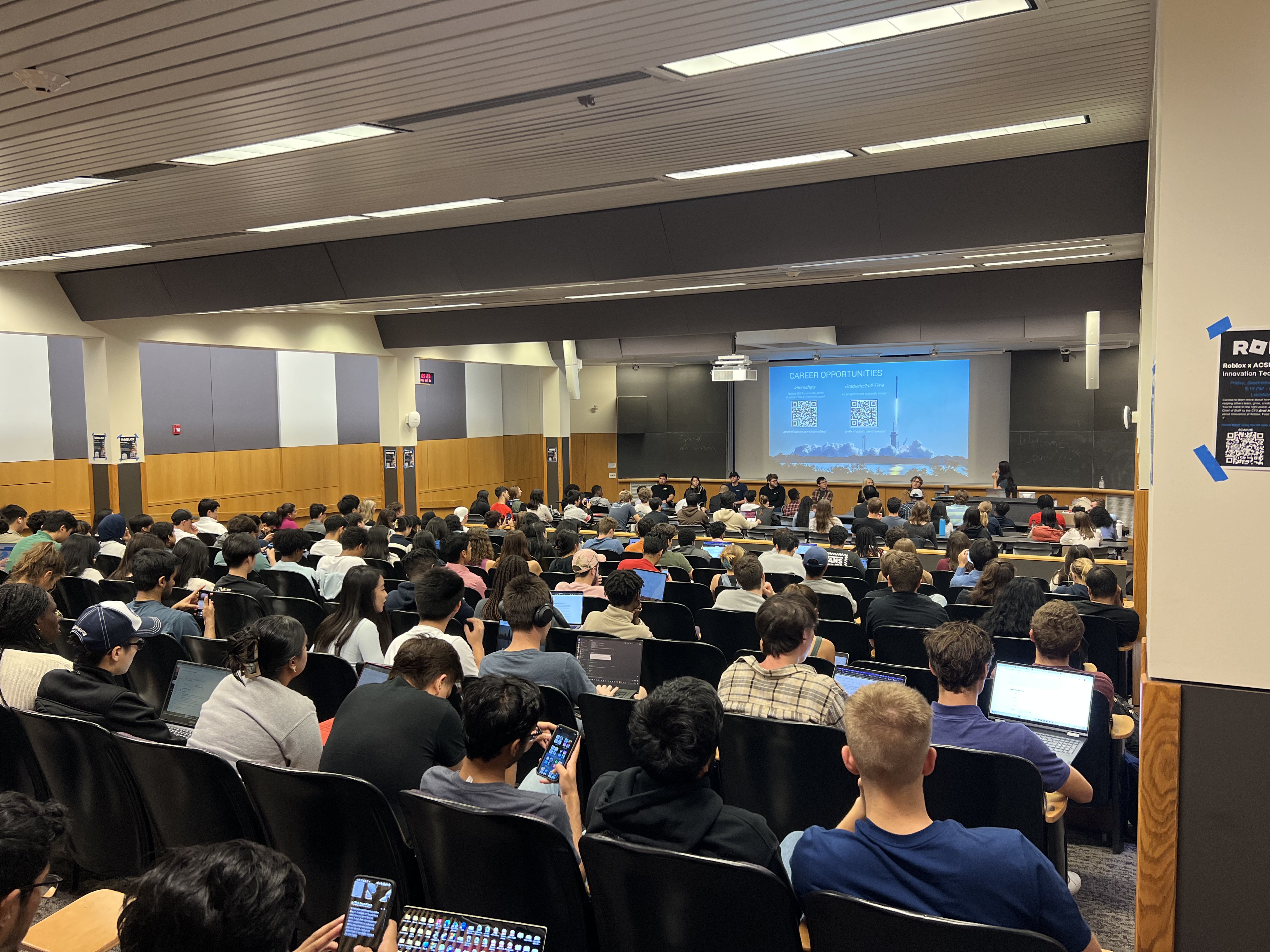 This image slider contains images of NSBE-CU's SpaceX Information Session. The first image of this slider displays an image, taken from the back of the lecture hall in which the event took place, of the congregation of Cornell students facing a panel of SpaceX recruiters.